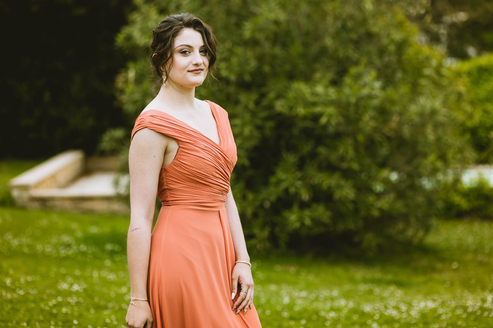 Invitée de mariage coiffée d'un chignon flou et maquillée, robe corail